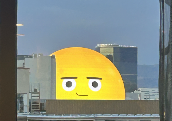 A photo taken out a hotel room window, looking at the Sphere in Las Vegas as it looms over a nearby building. It is showing the smirking emoji face.