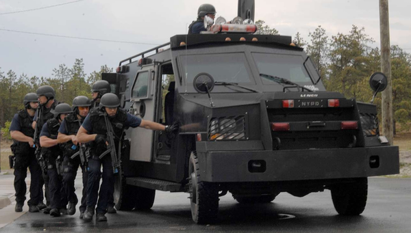 A photo of highly militarized police staging outside of an urban assault vehicle.